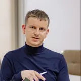 Andrei Stici, cu părul scurt, într-un pulover bleumarin cu guler înalt, ținând un pix